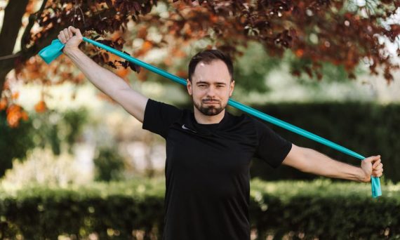 Adult man in black shirt exercises with a resistance band outside.