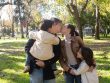 A joyful family sharing a tender moment in a sunny park setting.
